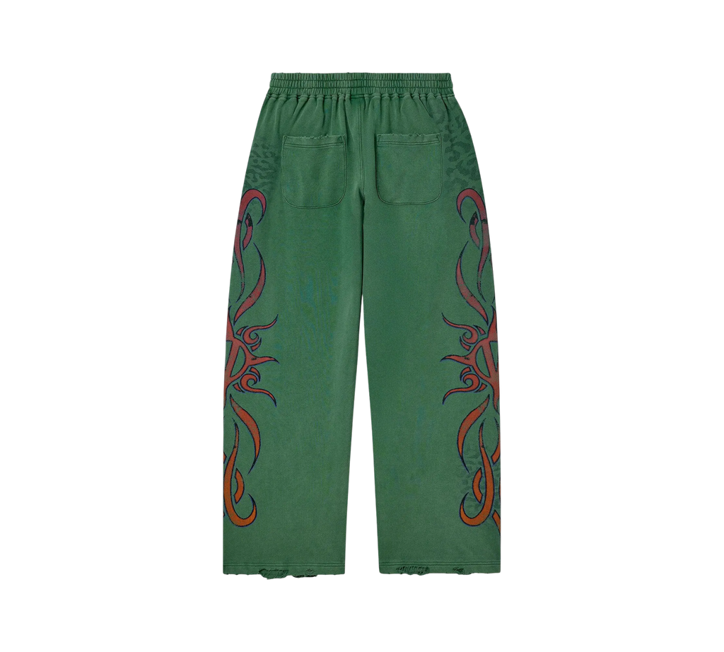 Genesis Boutique Vale Inferno green wide-fit sweatpants with red tribal flame graphics and distressed hem details.