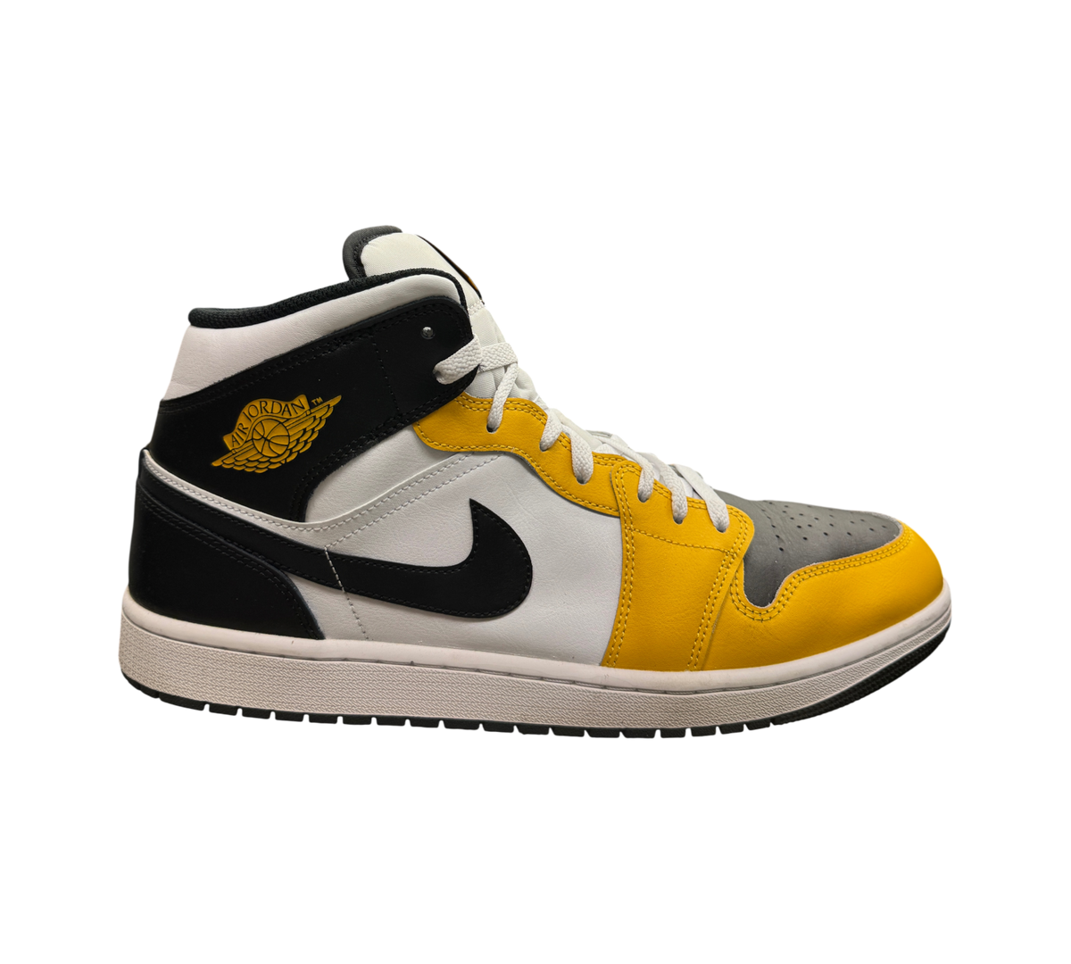 Genesis Boutique Jordan 1 Mid Yellow Ochre sneakers featuring black, white, and yellow leather panels on a glass shelf