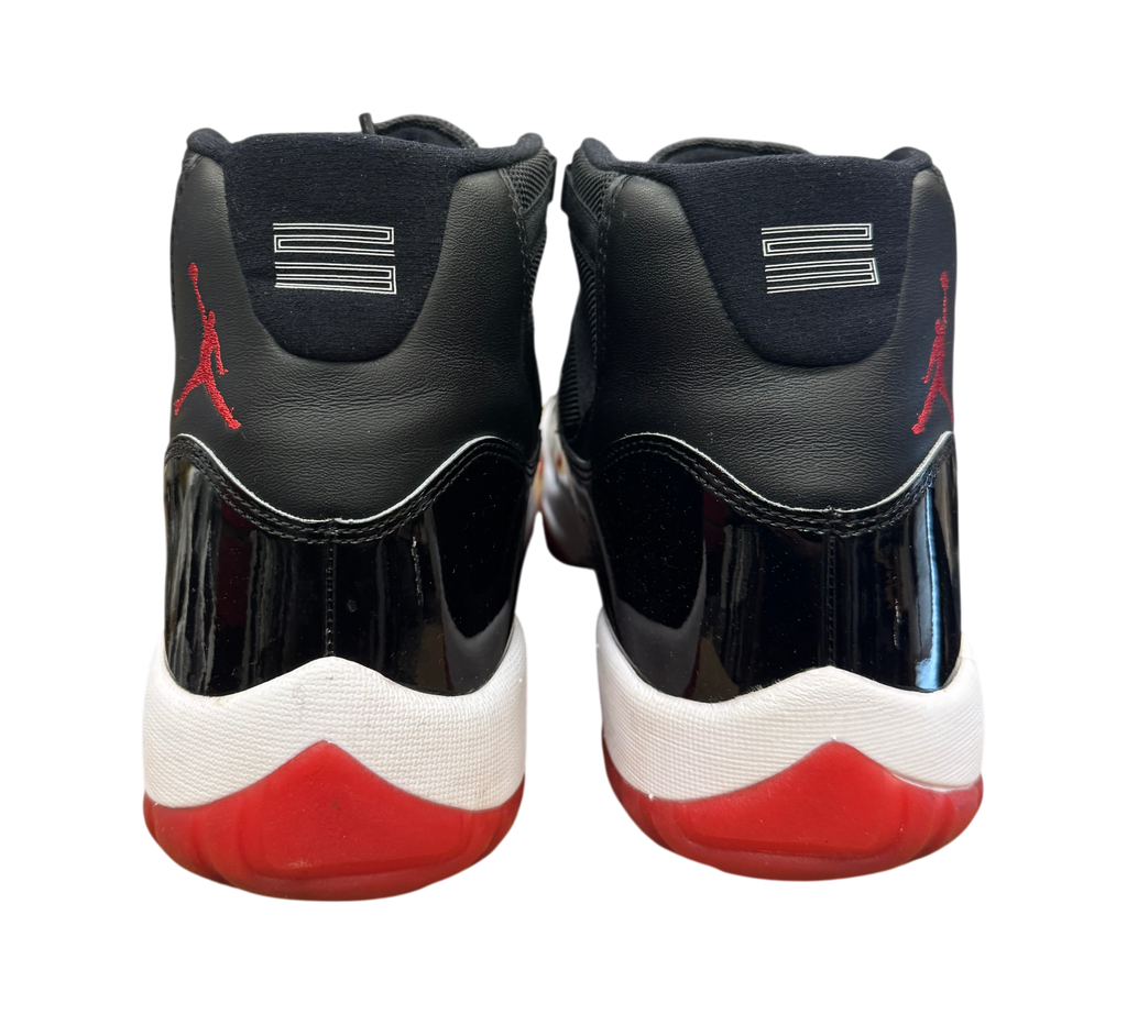 Genesis Boutique Jordan 11 Bred sneakers showing the black patent leather heel, red Jumpman logo, and white midsole.