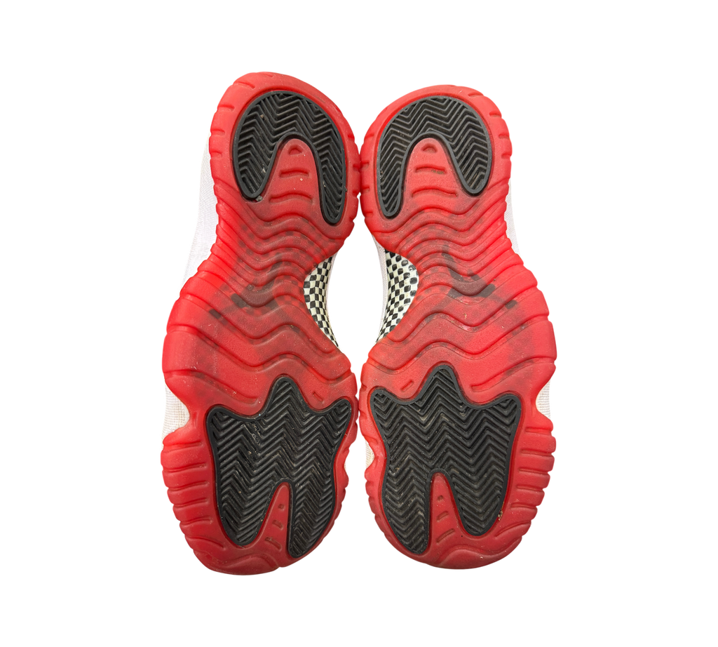 Genesis Boutique Jordan 11 GS Bred sneakers showing the red and black rubber outsoles with carbon fiber plate detail