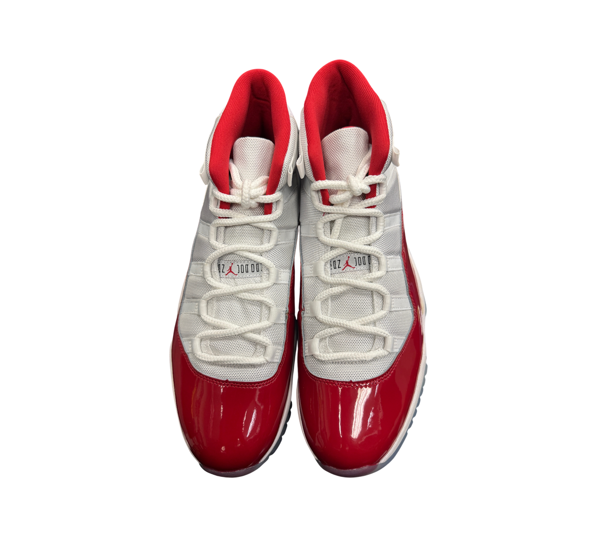 Genesis Boutique Jordan 11 Cherry sneakers featuring white mesh uppers, red patent leather mudguards, and red lining.