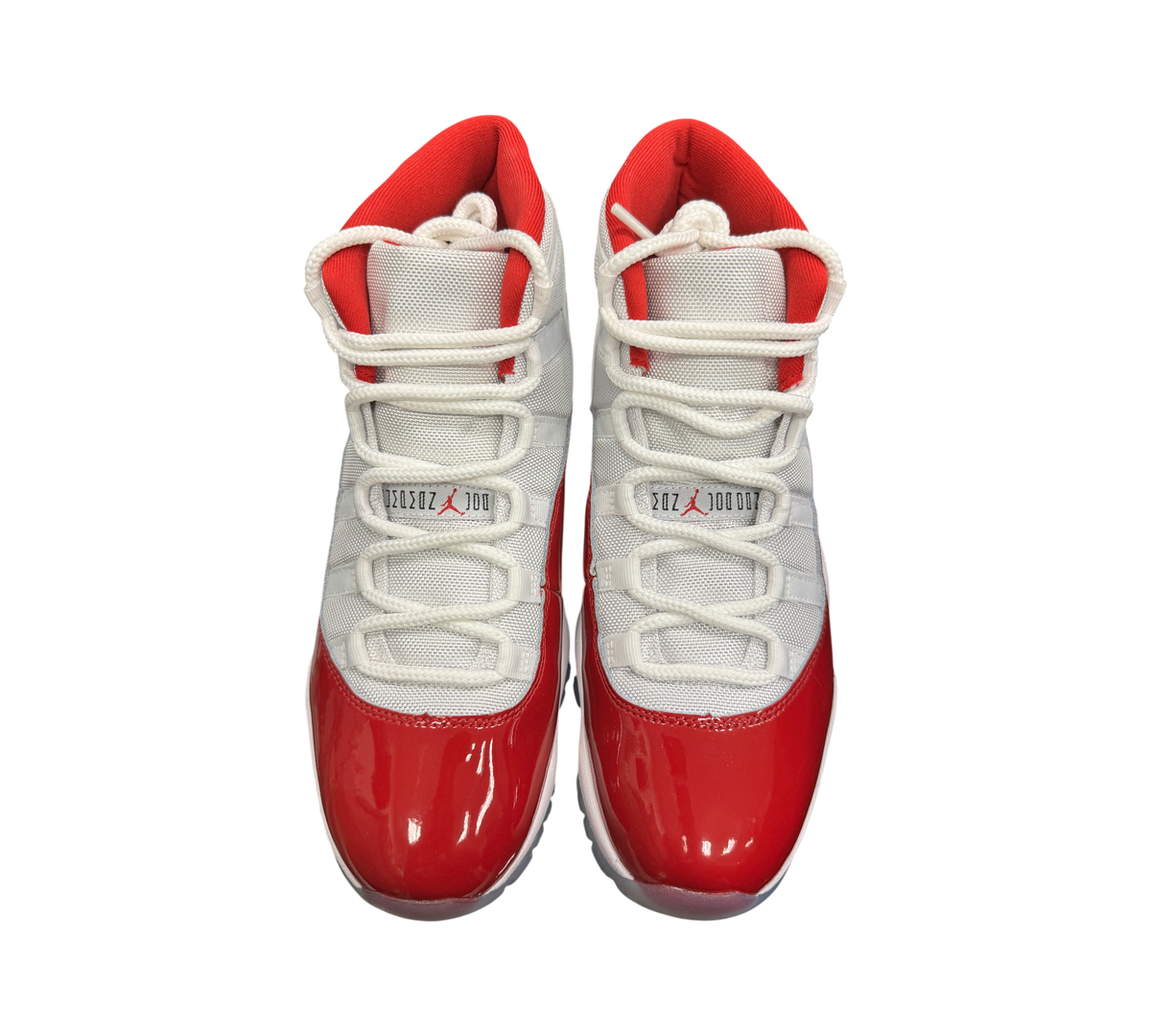 Genesis Boutique Jordan 11 Cherry sneakers featuring white mesh uppers and glossy red patent leather mudguards.