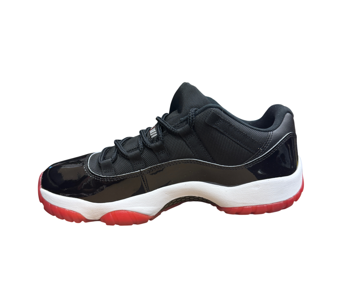 Genesis Boutique Jordan 11 Low Bred sneaker with black mesh upper, patent leather mudguard, and red rubber outsole.