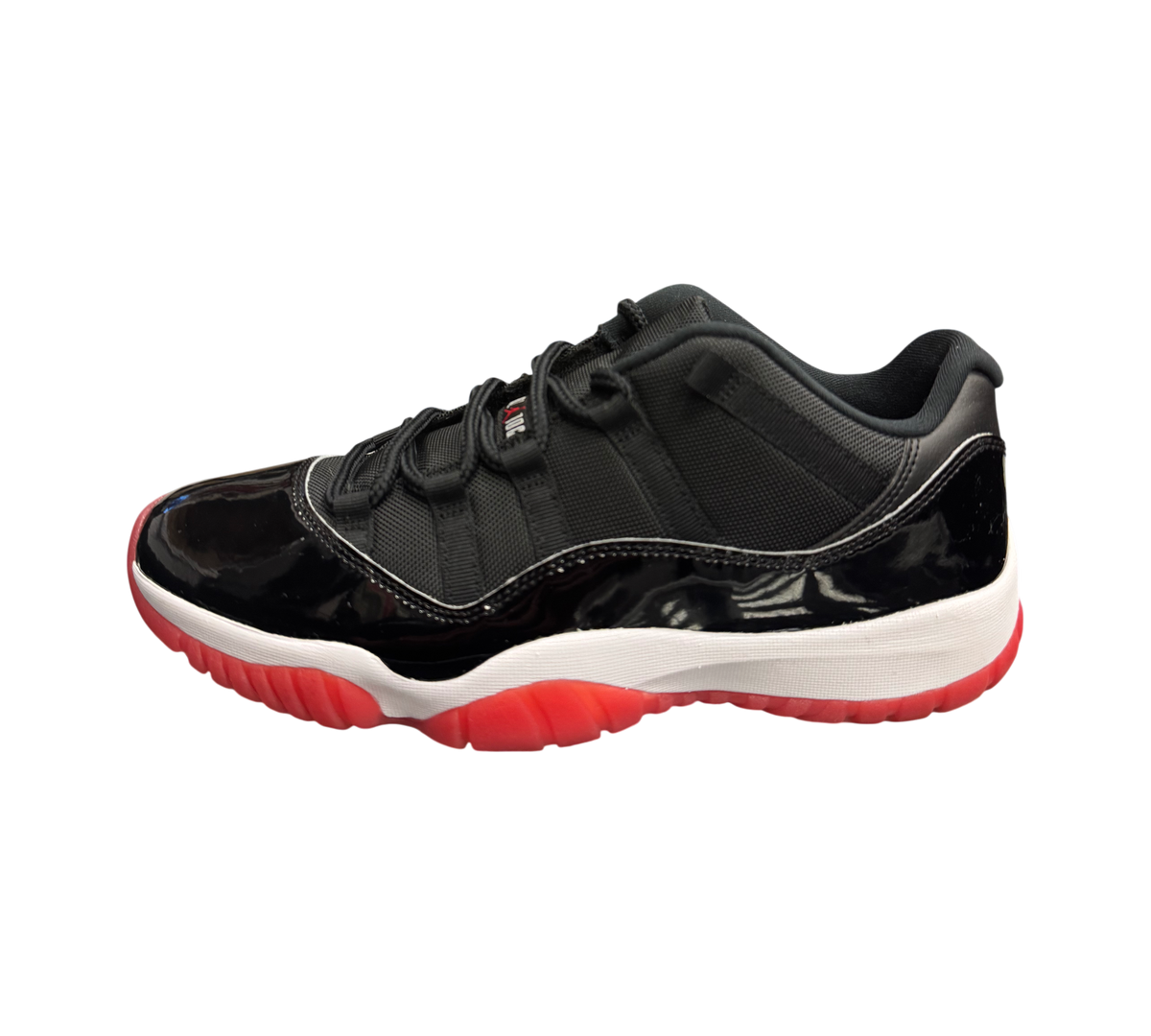 Genesis Boutique Jordan 11 Low Bred sneakers featuring black patent leather, mesh upper, and a red translucent outsole.