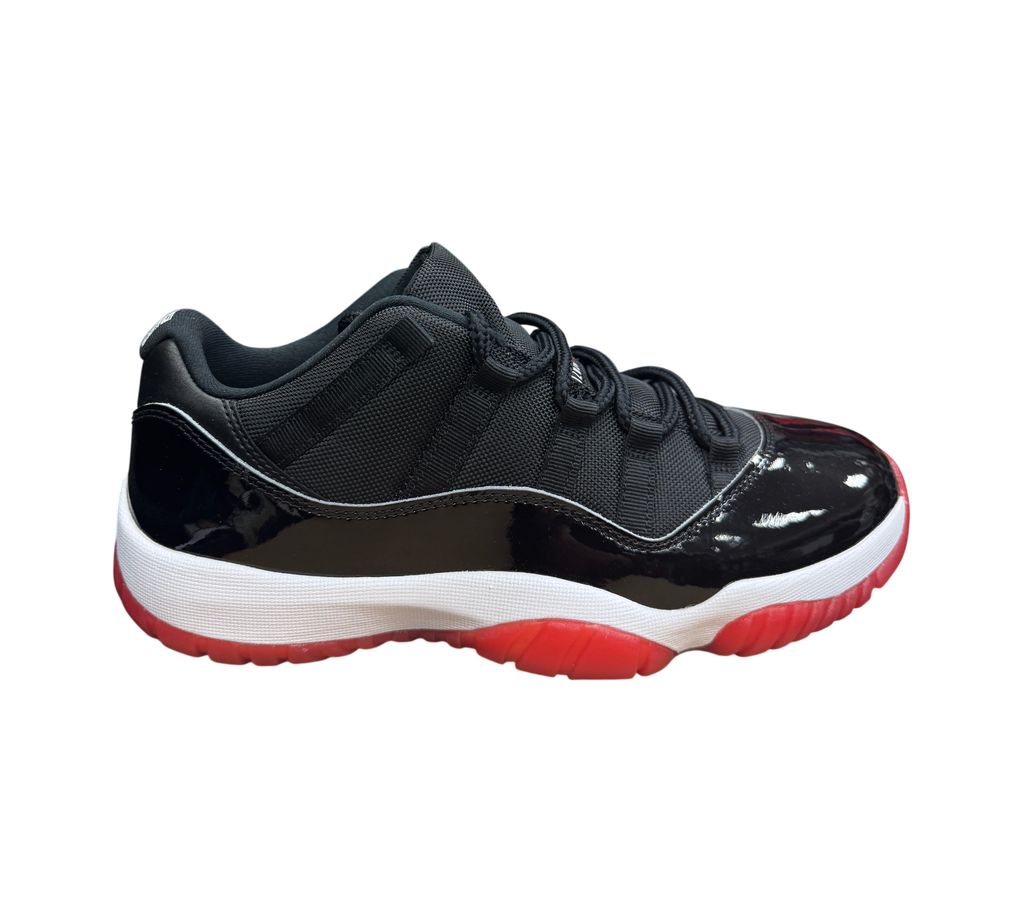Genesis Boutique Jordan 11 Low Bred sneaker featuring black mesh upper, patent leather mudguard, and red outsole.
