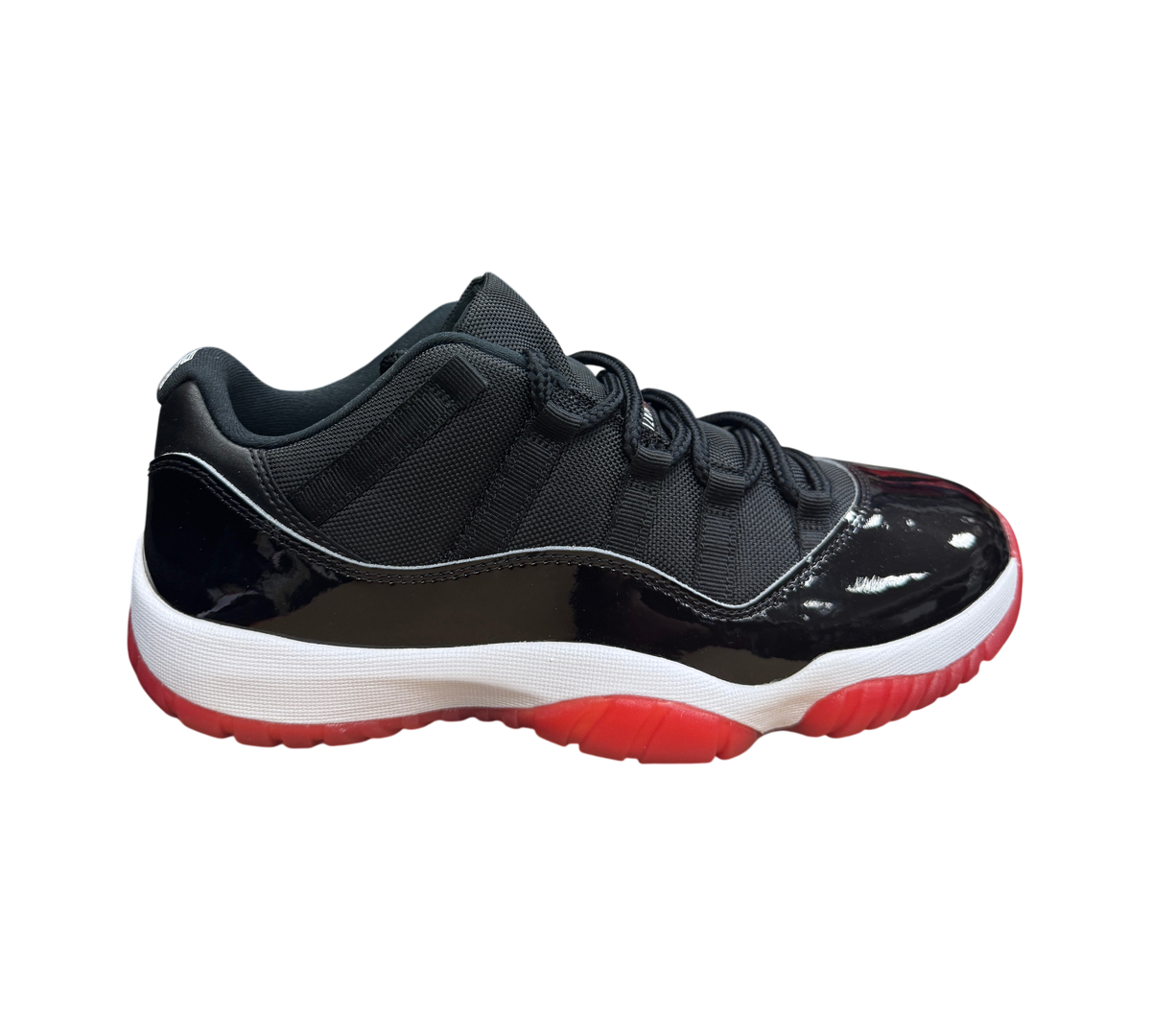 Genesis Boutique Jordan 11 Low Bred sneaker featuring black mesh upper, patent leather mudguard, and red outsole.