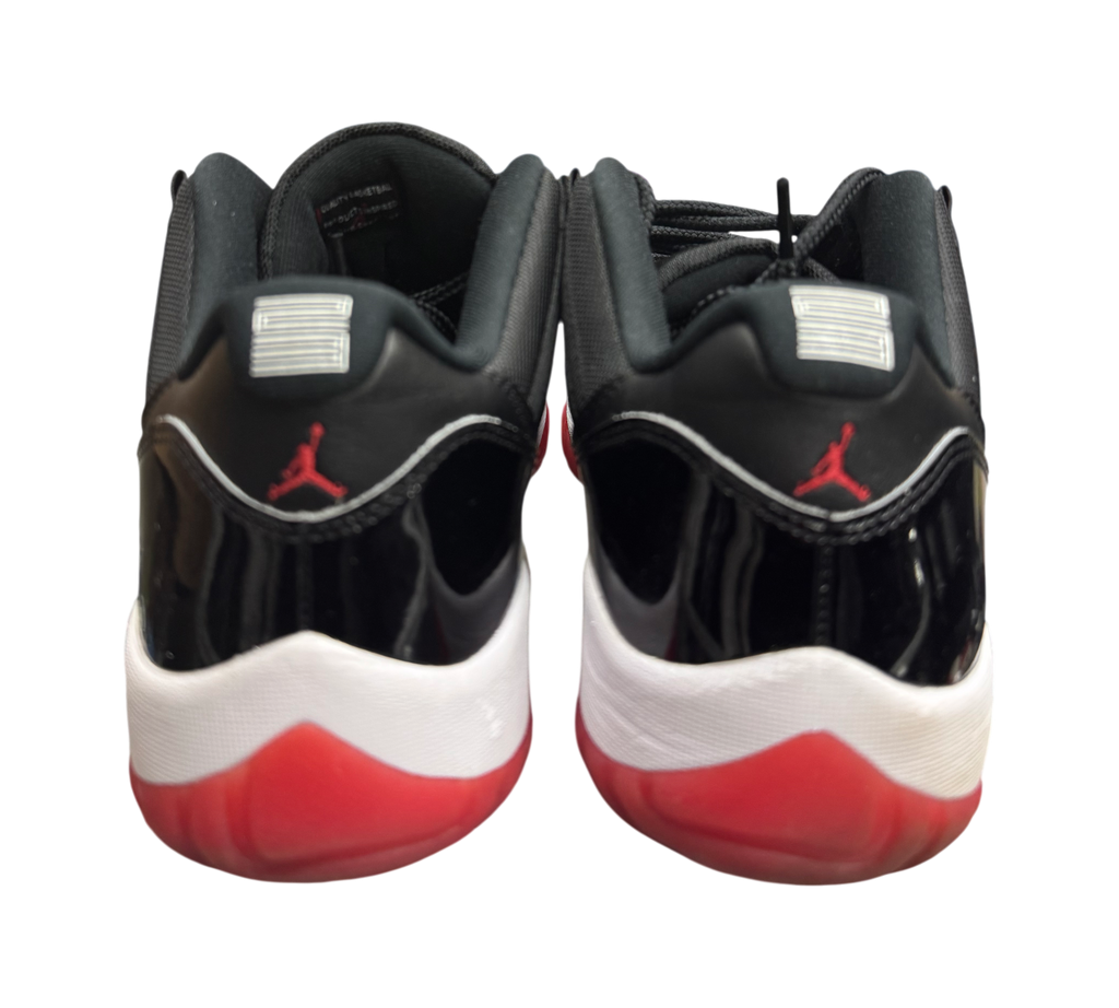 Genesis Boutique Jordan 11 Low Bred sneakers featuring black patent leather, red outsoles, and Jumpman branding.