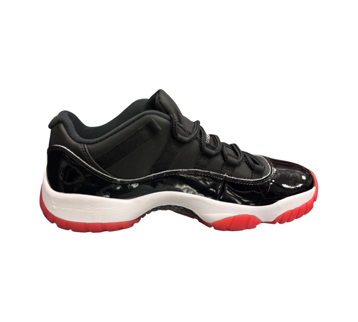 Genesis Boutique pre-owned Jordan 11 Low Bred sneakers featuring black patent leather, mesh upper, and red outsole.