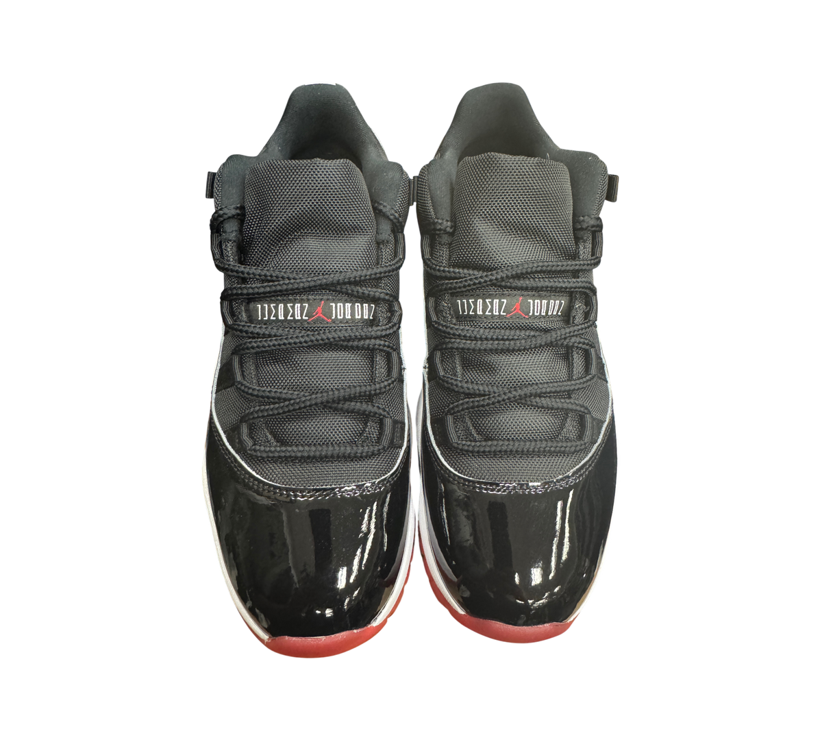Genesis Boutique pre-owned Jordan 11 Low Bred sneakers featuring black patent leather, mesh upper, and red outsole.