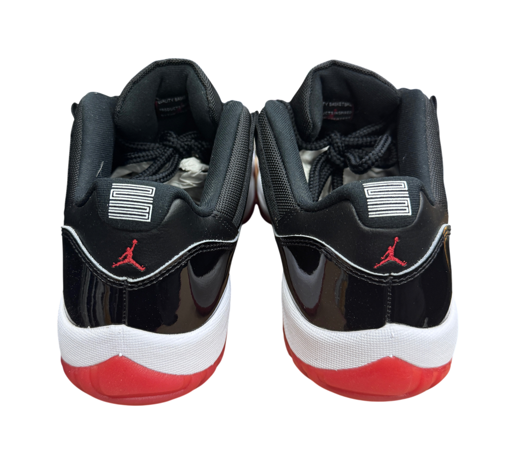Genesis Boutique Jordan 11 Low Bred sneakers featuring black patent leather, red accents, and number 23 heel detail.
