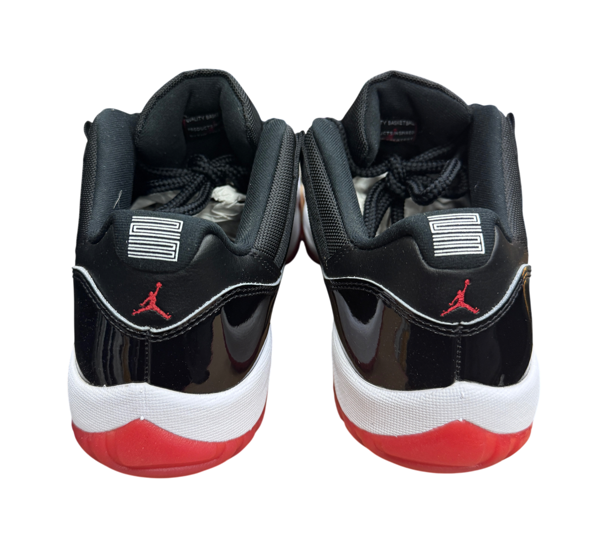 Genesis Boutique Jordan 11 Low Bred sneakers featuring black patent leather, red accents, and number 23 heel detail.