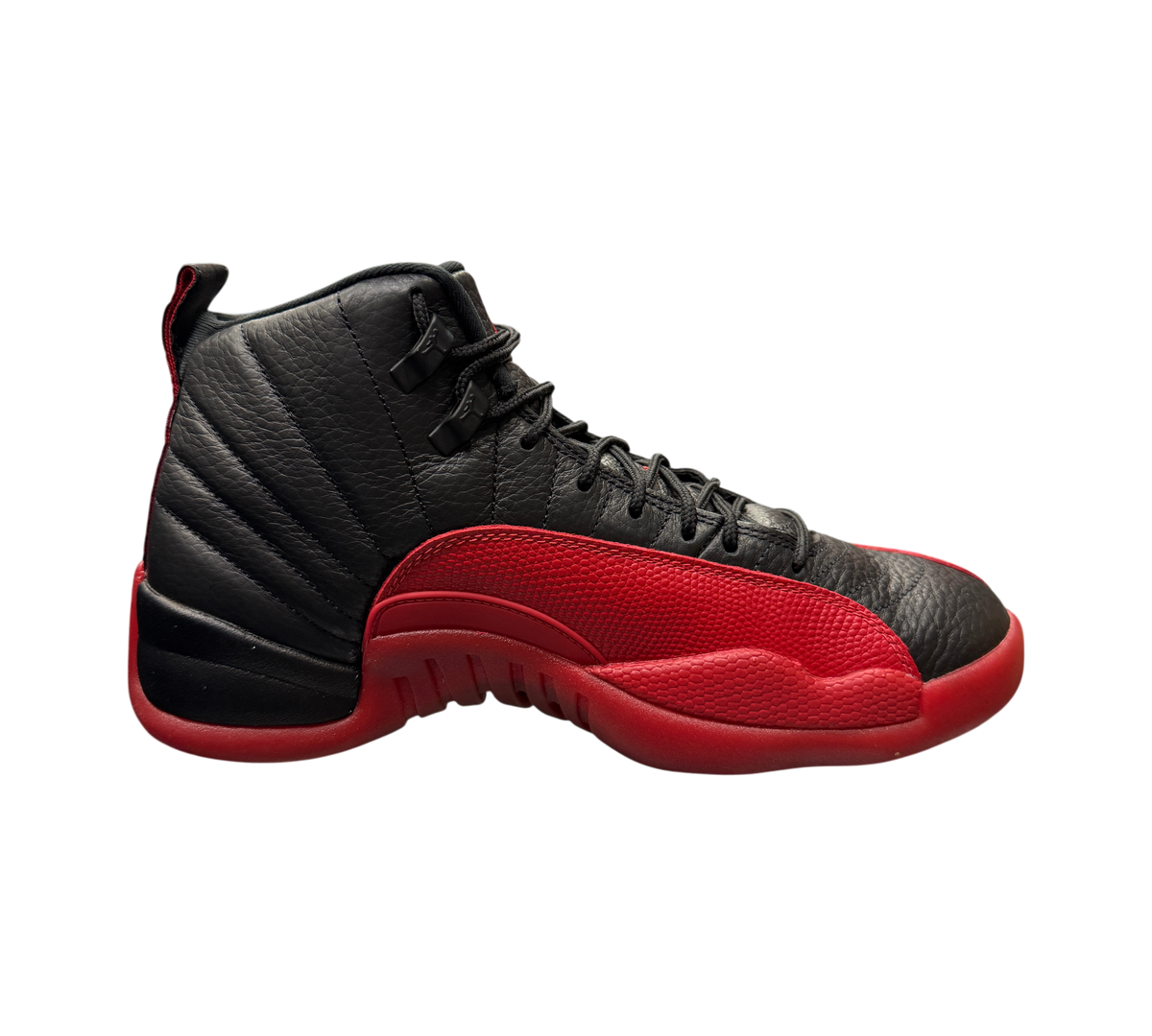 Genesis Boutique Jordan 12 Flu Game 2025 sneakers in black and red leather displayed on a glass shelf in a store