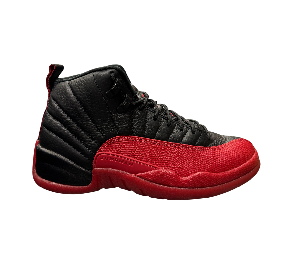 Genesis Boutique Jordan 12 Flu Game 2025 sneakers in black and red leather displayed on a glass shelf in a store.