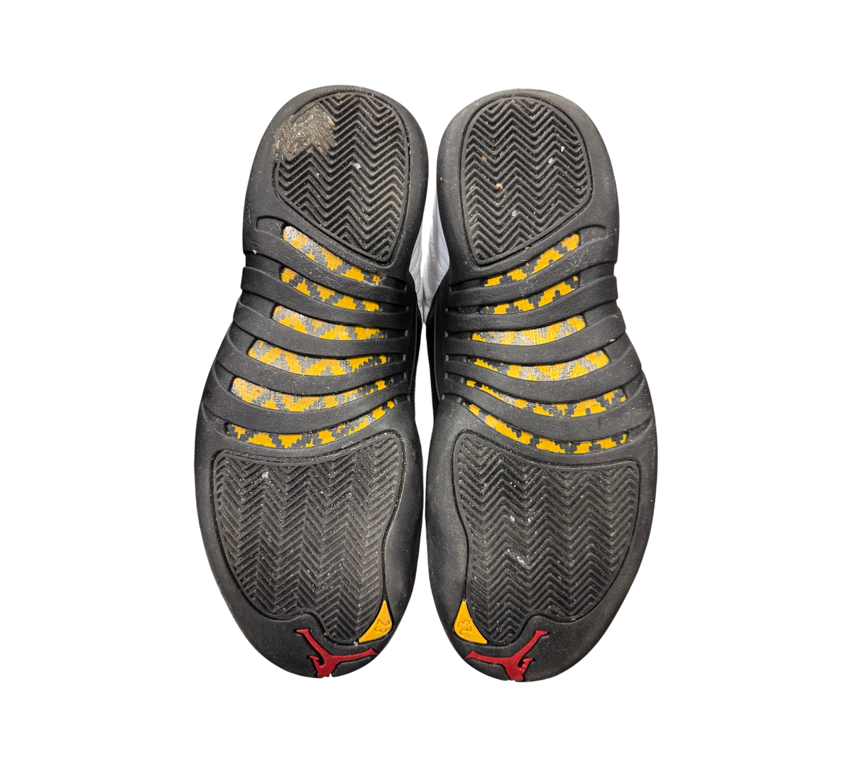 Used Jordan 12 Taxi sneakers from Genesis Boutique showing black and yellow herringbone outsoles with red Jumpman logo.