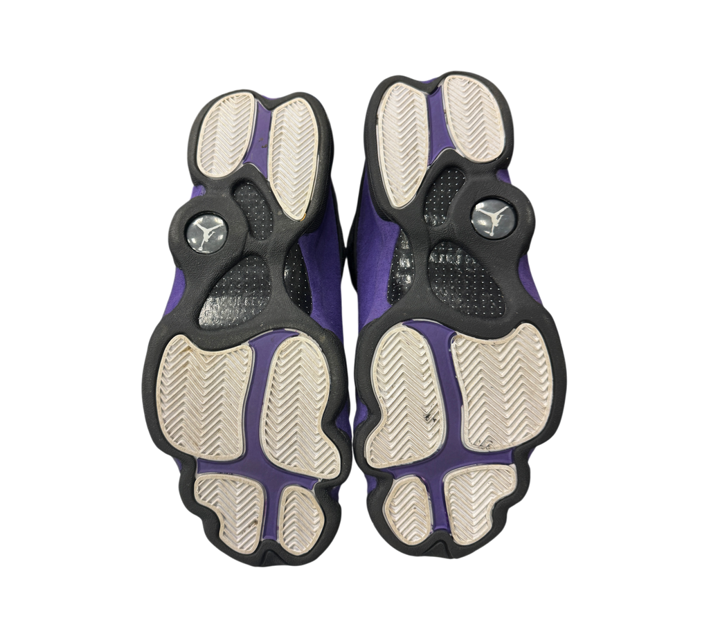 Genesis Boutique Jordan 13 Court Purple sneakers showing the black and purple patterned outsoles from below.