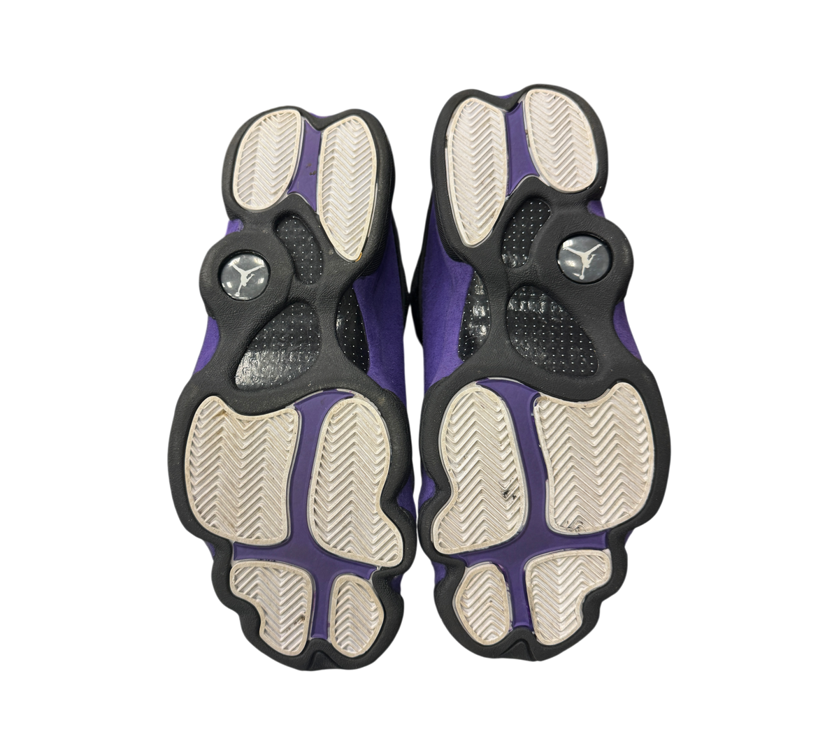 Genesis Boutique Jordan 13 Court Purple sneakers showing the black and purple patterned outsoles from below.