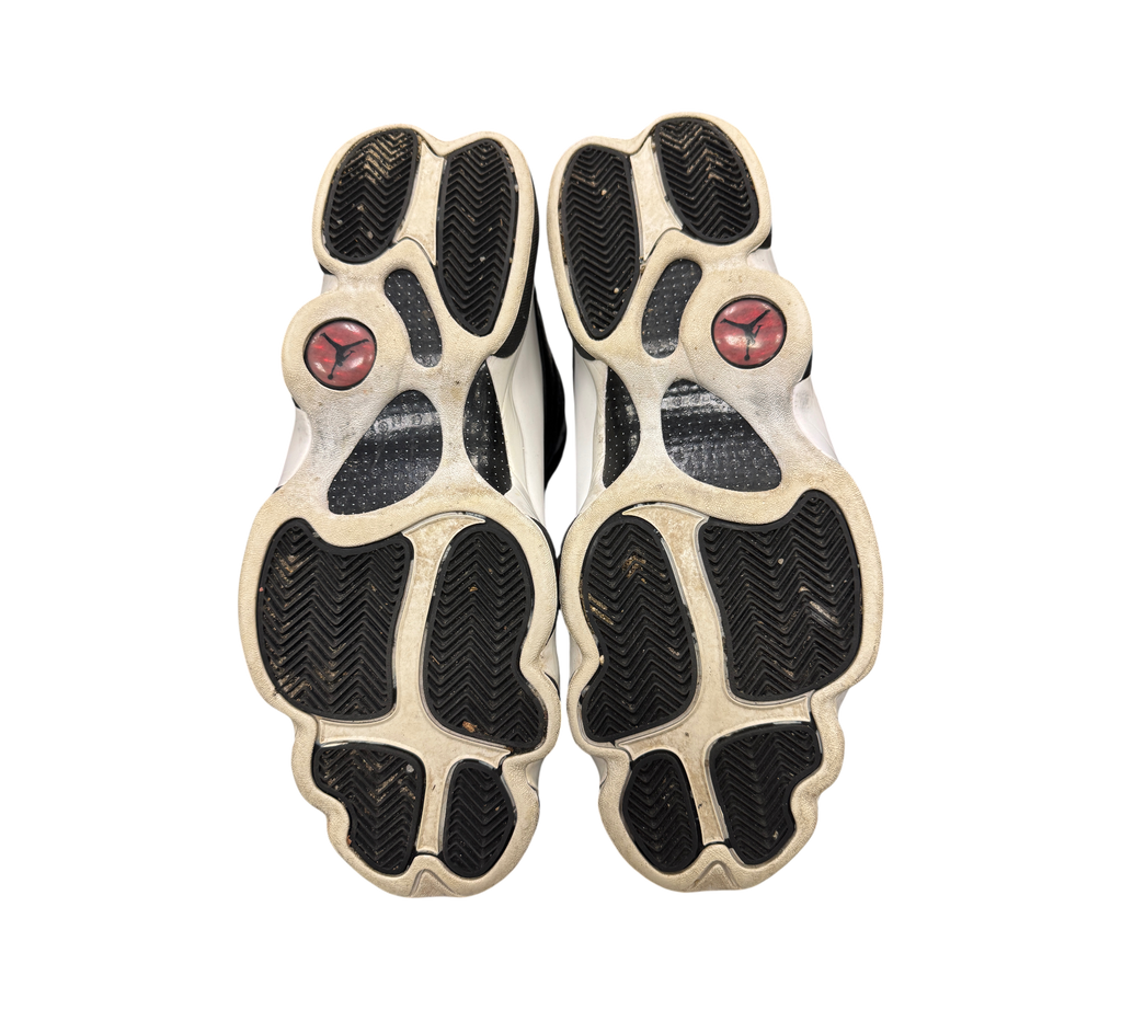 Genesis Boutique Jordan 13 Reverse He Got Game sneakers showing the black and white treaded outsoles with red logos.