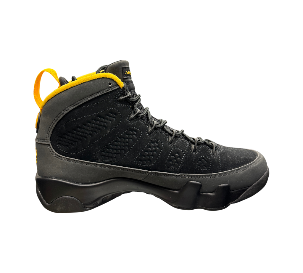 Genesis Boutique Jordan 9 Charcoal high-top sneaker in black suede with yellow heel pull tab on a glass display case