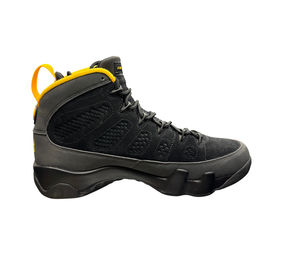 Genesis Boutique Jordan 9 Charcoal high-top sneaker in black suede with yellow heel pull tab on a glass display case